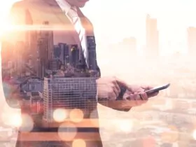 The double exposure image of the business man using a smartphone during sunrise overlay with cityscape image. The concept of modern life, business, city life and internet of things.
